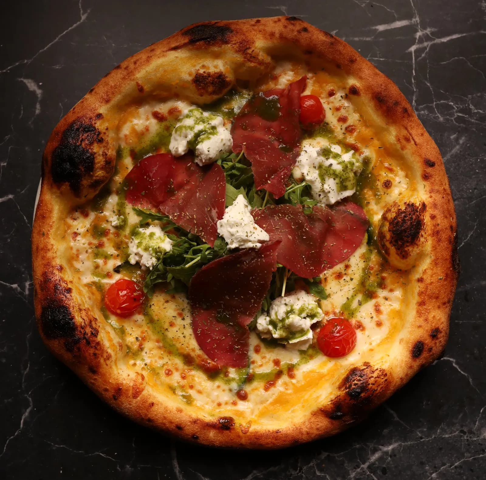 Holzofenpizza mit Bresaola, Burrata, Rucola, Kirschtomaten und Pesto