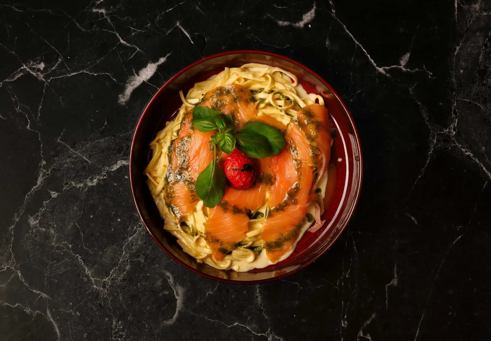 Tagliatelle mit Räucherlachs, Basilikumpesto und gerösteter Kirschtomate auf dunklem Marmor
